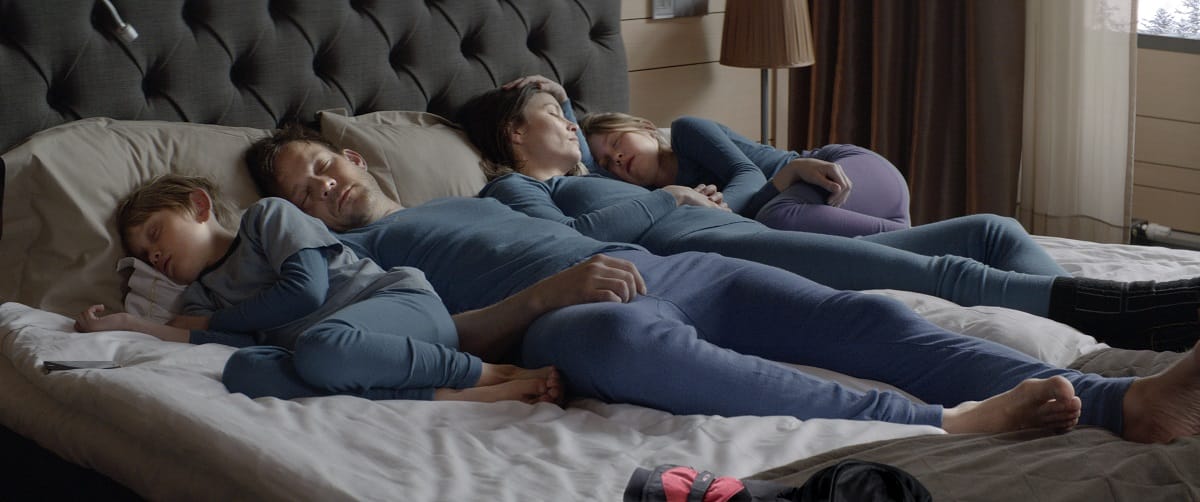 Still from Force Majeure. A family of four is sleeping in a hotel bed, all wearing identical blue ski underclothes.